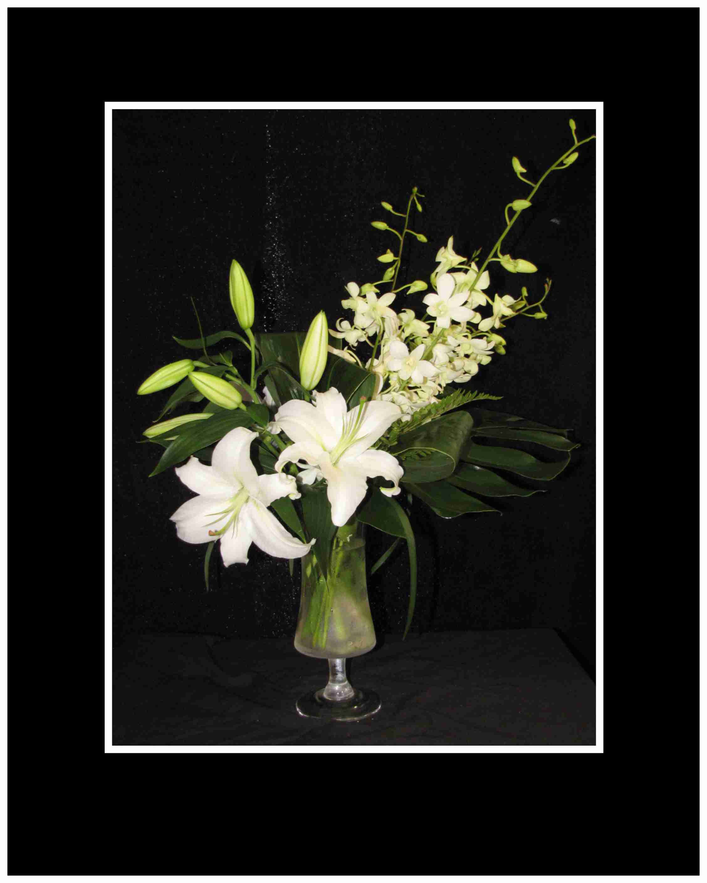 White lilies and orchids arranged in a glass vase