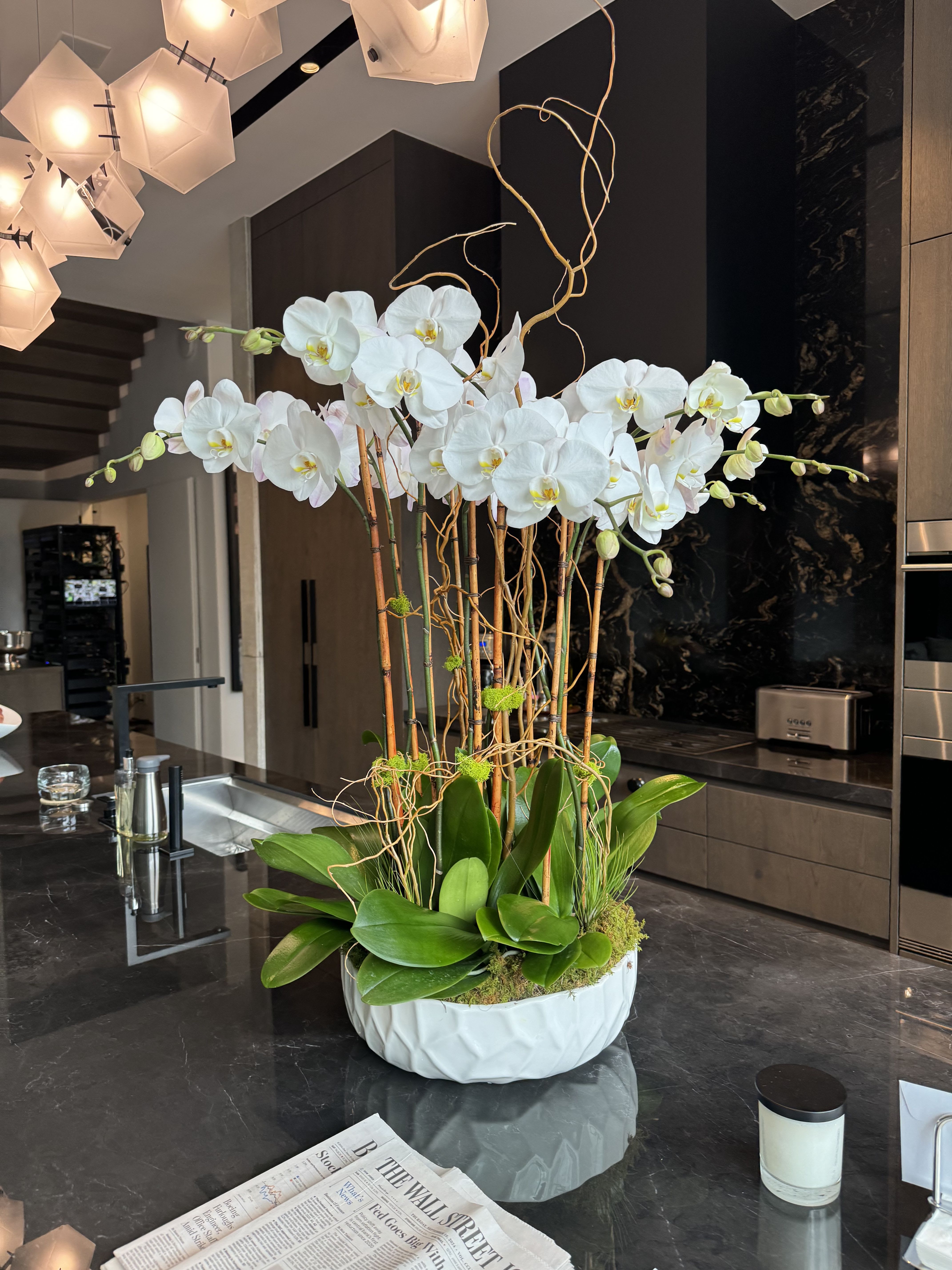Tall white orchid arrangement in a white bowl-shaped vase