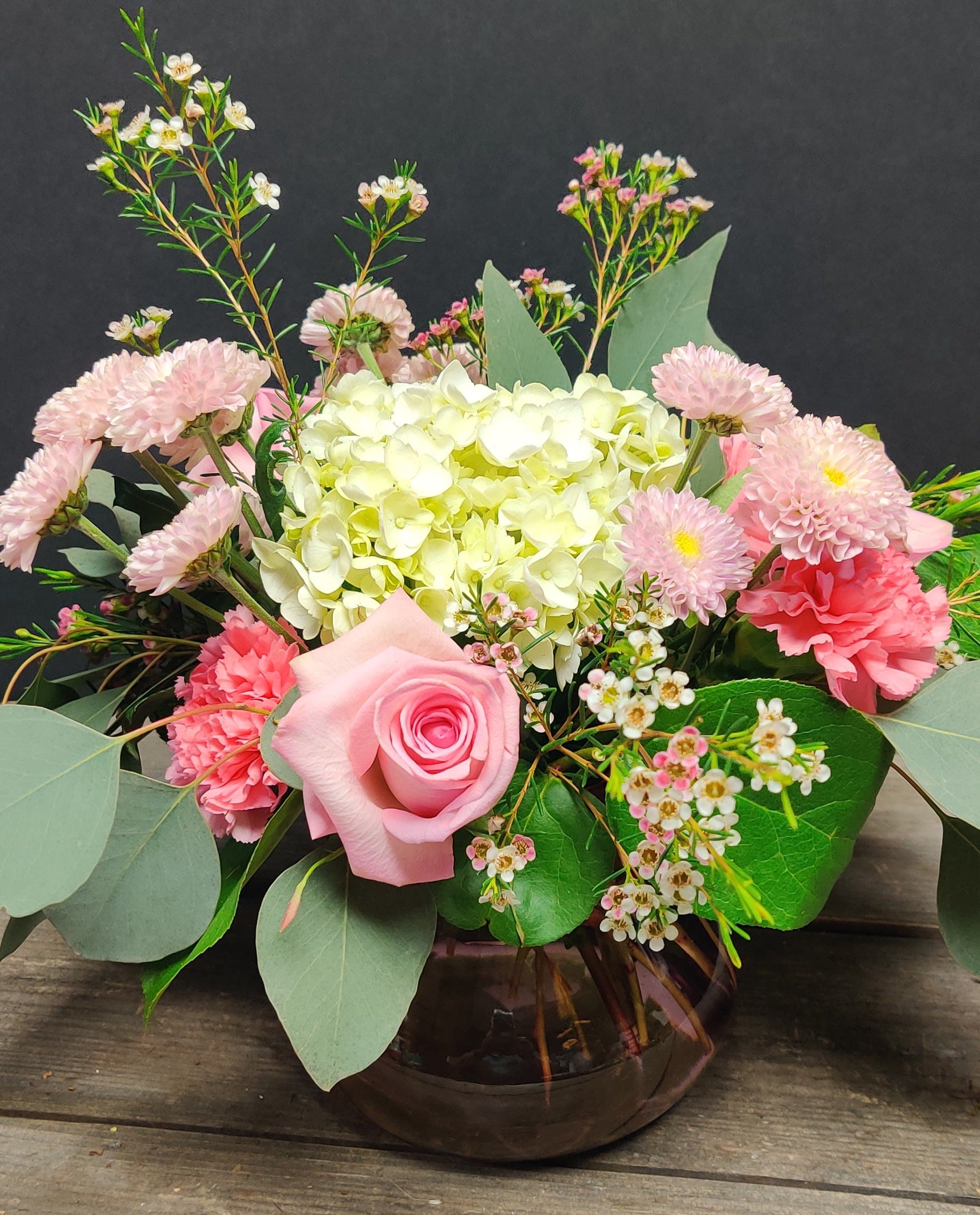 Low arrangement of pink roses, carnations, mums, and white hydrangea in a round glass vase