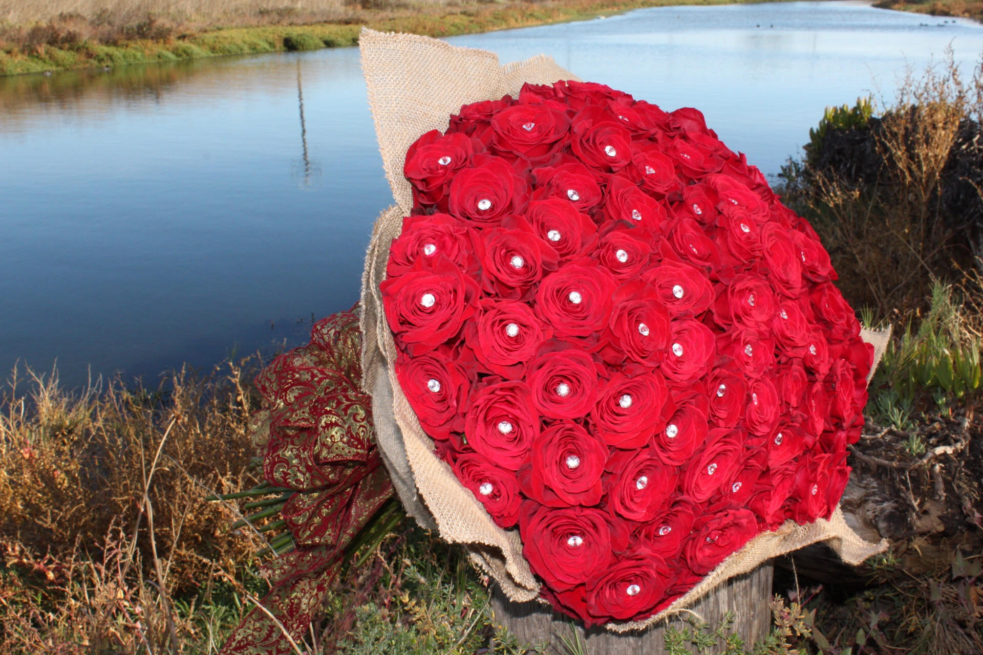 Grand Red Love by D'Lily's Flowers  - This magnificent hand bouquet holds 7 dozens of the highest quality red roses! It is truly breath-taking.   Regular holds 5 dozens. Deluxe holds 7 dozens, as shown in the picture. Premium holds 10 dozens. Disclaimer: This is a wrapped bouquet. No Vase is Included. 