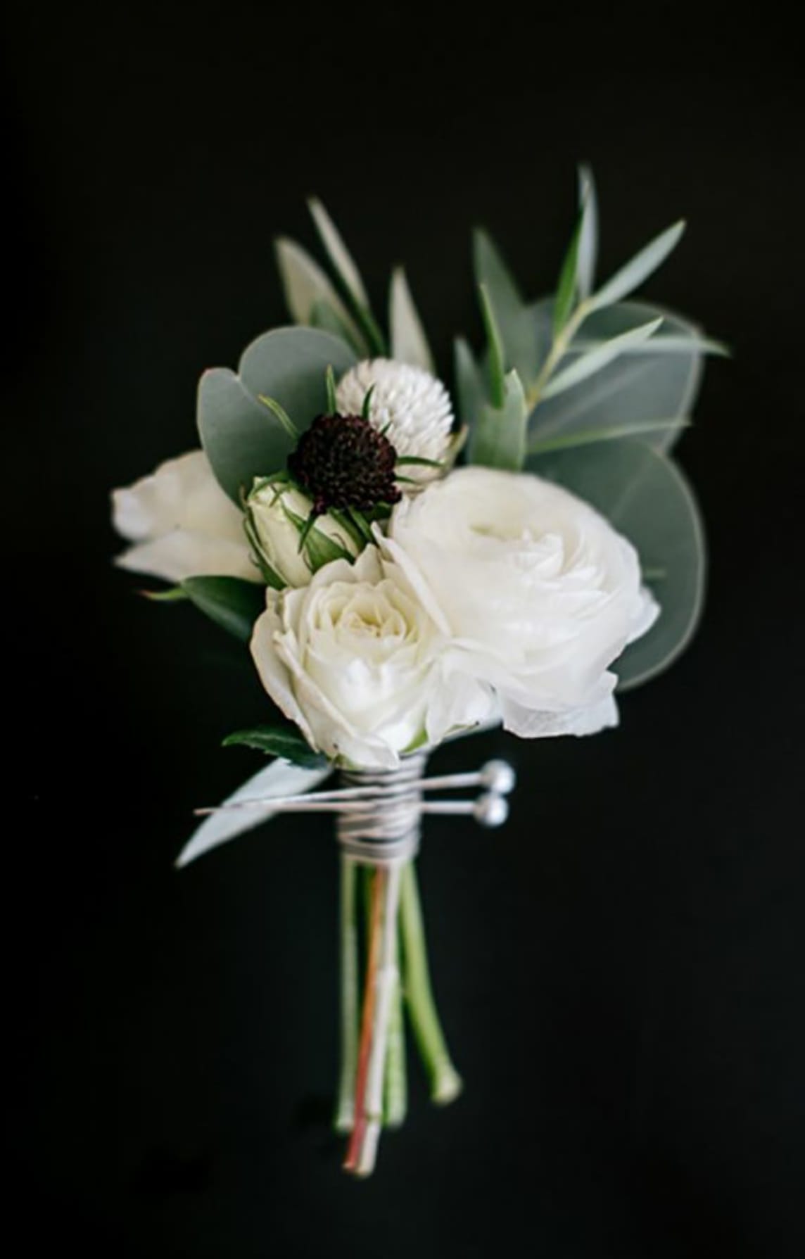 Small white floral boutonniere with eucalyptus on a black background