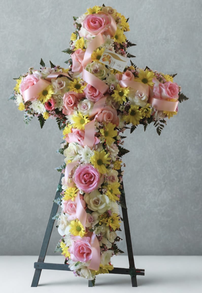 Cross-shaped floral arrangement with pink roses and yellow daisies on an easel