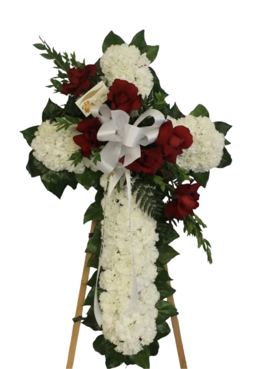 Standing white floral cross with red roses and white bow on an easel