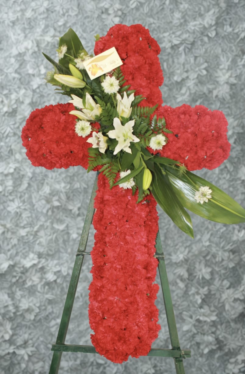 Red floral cross on a stand with white lilies and greenery