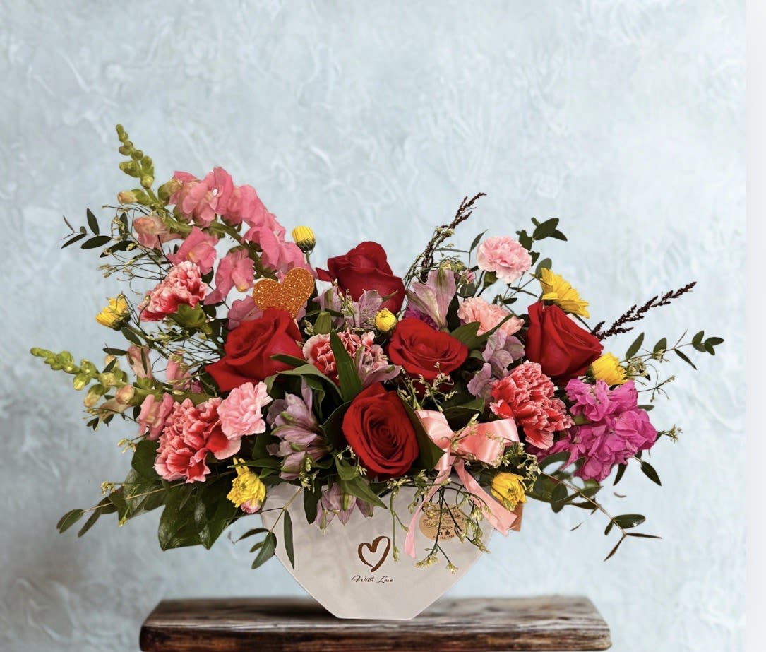 Cupid’s Garden  - Inspired by a blooming spring garden, this arrangement combines passionate red roses, ruffled pink blooms, and cheerful yellow flowers. With playful heart accents and graceful movement, Cupid’s Garden delivers charm, warmth, and romance in every detail.