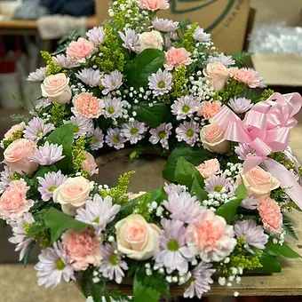 Pastel floral wreath with roses, daisies, and carnations on a pink ribbon