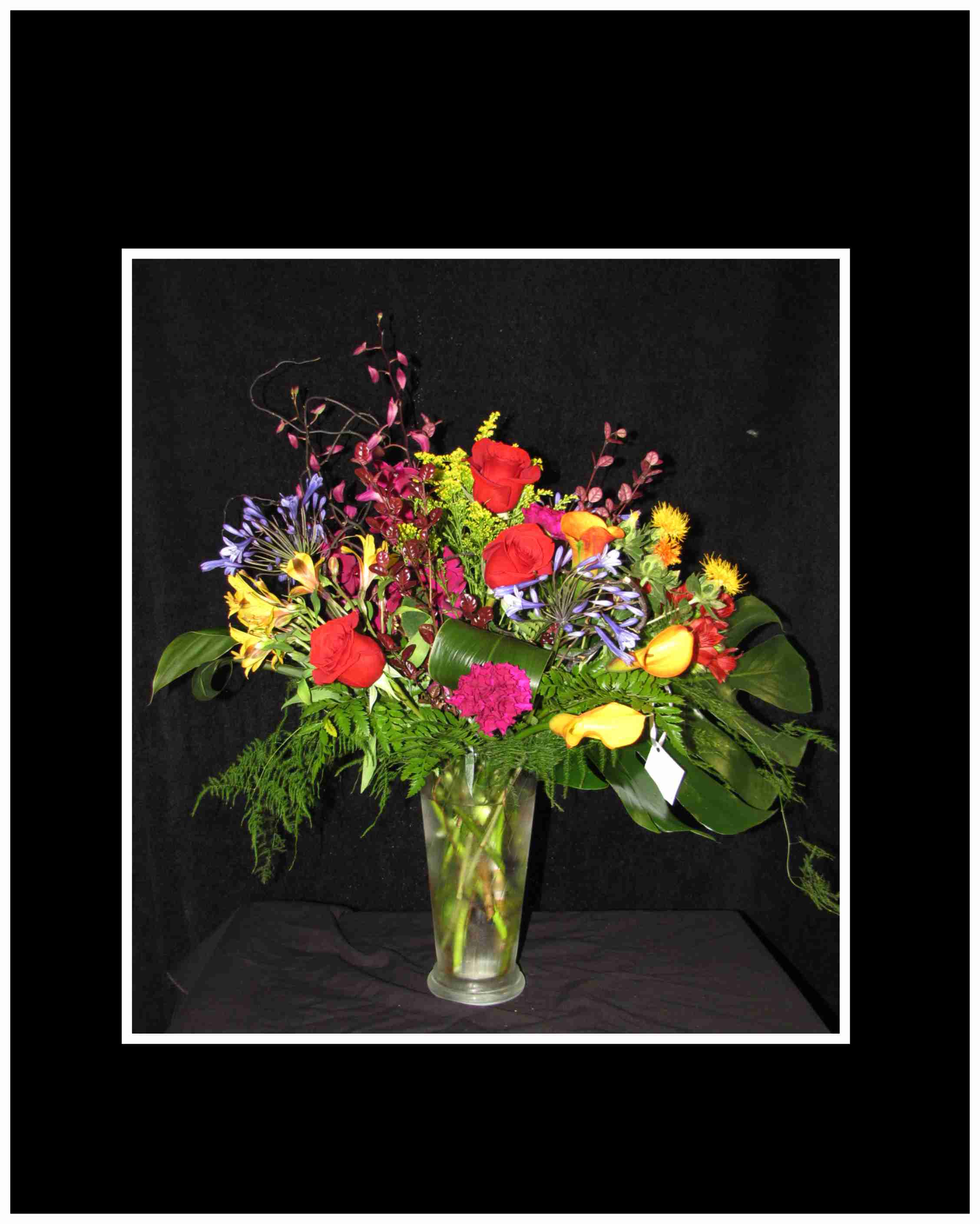 Mixed bouquet of red roses and colorful flowers in a clear glass vase