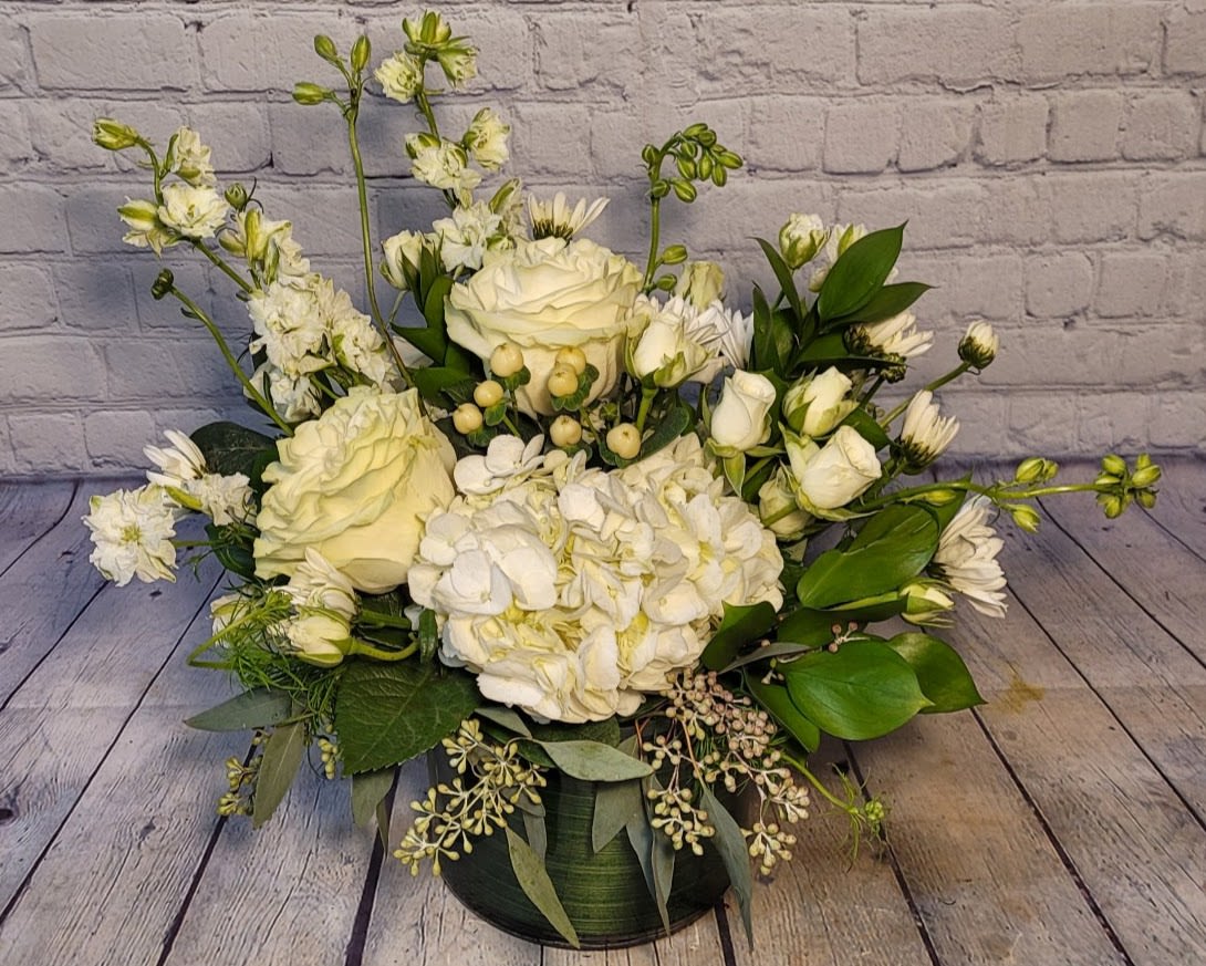 White roses and hydrangeas in a low green vase with mixed greenery