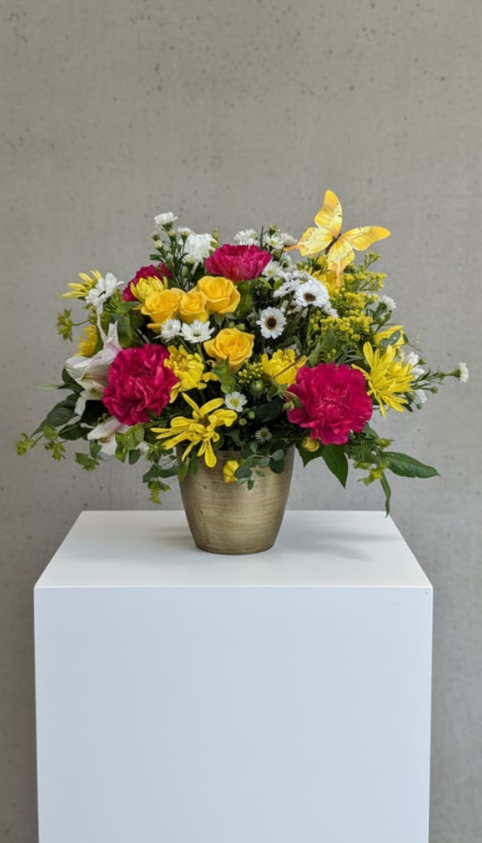 Bright mixed flower arrangement in a gold vase with a yellow butterfly accent.