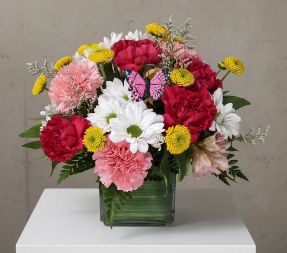Mixed bouquet of pink, red, white, and yellow flowers in a square glass vase