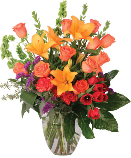 Mixed bouquet of orange lilies, roses, and red flowers in a glass vase
