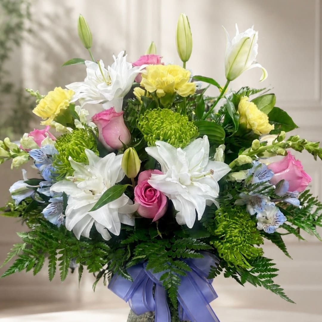 Bouquet of white lilies, pink roses, and yellow carnations in a vase with a purple ribbon