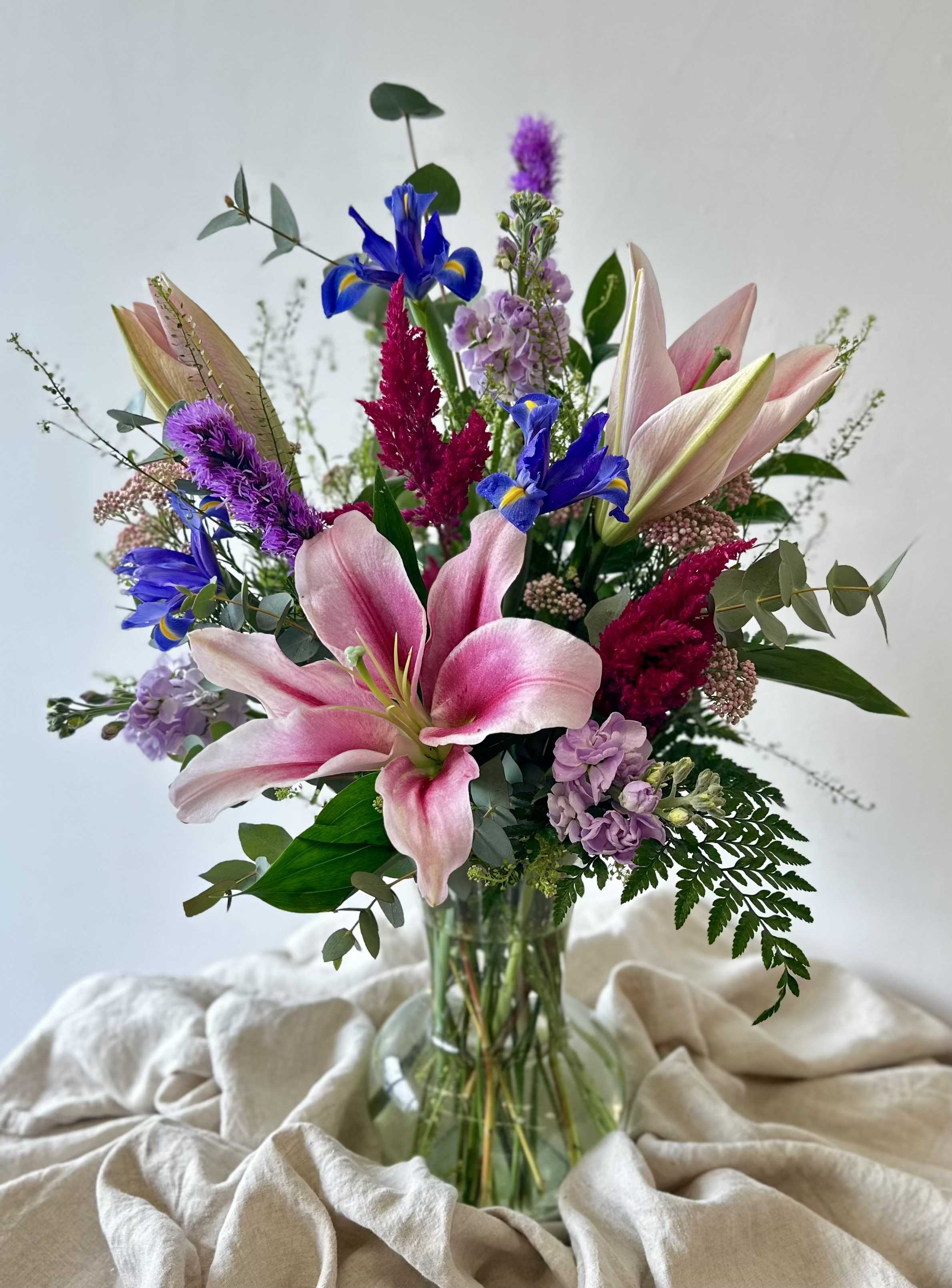 Mixed bouquet with pink lilies, blue irises, and purple flowers in a glass vase