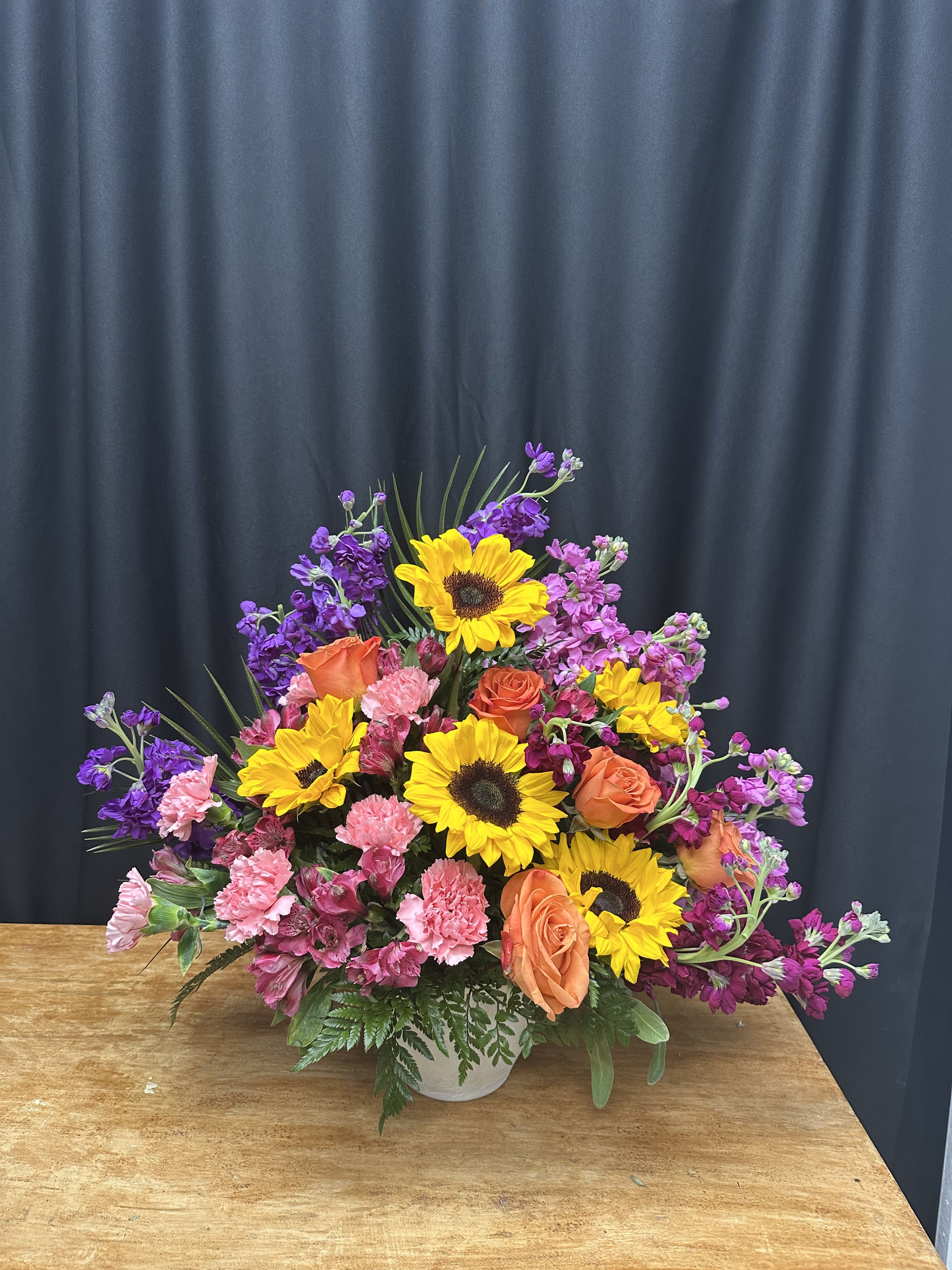 Mixed bouquet with sunflowers, orange roses, and pink carnations in a white vase