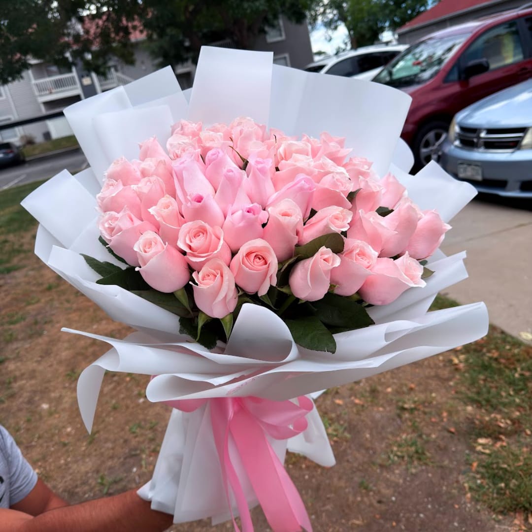 Bouquet of pale pink roses wrapped in white paper with a pink ribbon