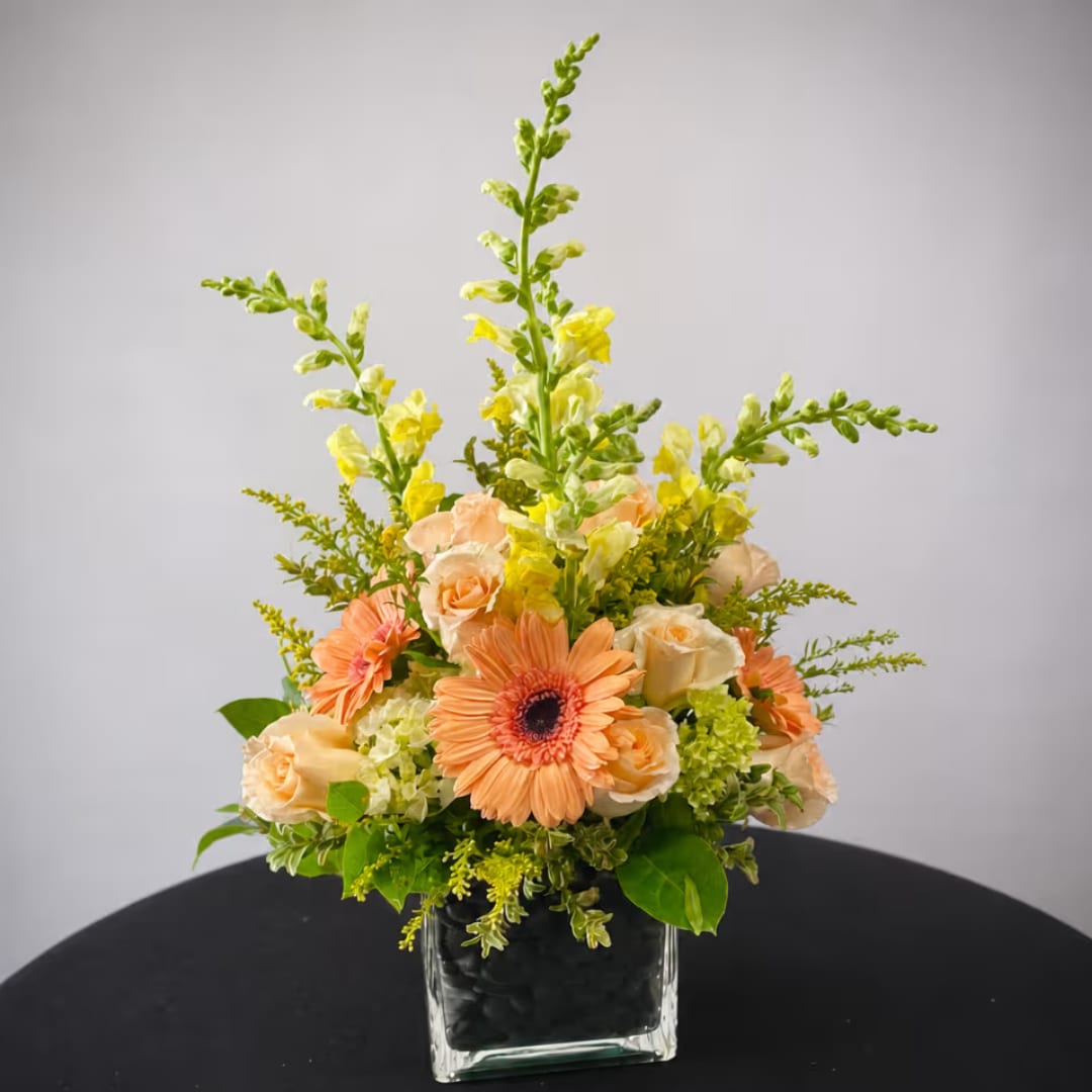 Peach gerbera daisies and roses in a square glass vase