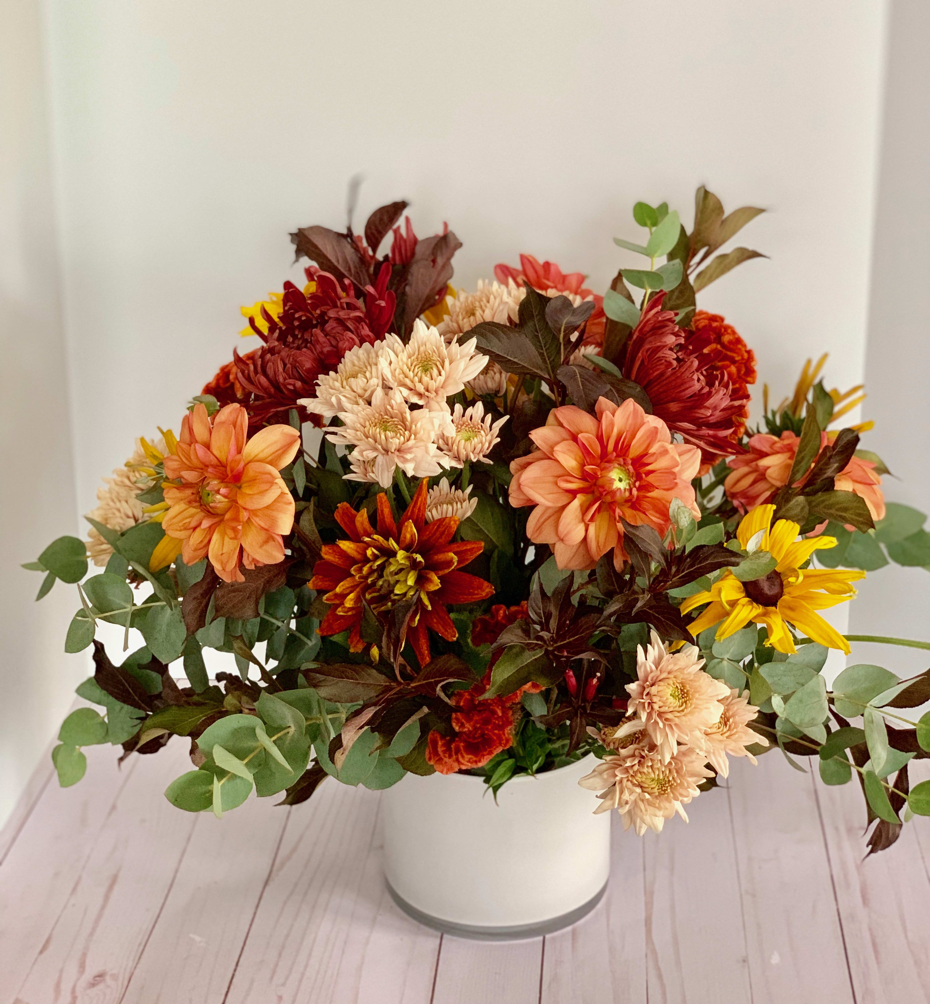 Mixed autumn bouquet in a white vase with orange, red, yellow, and cream blooms