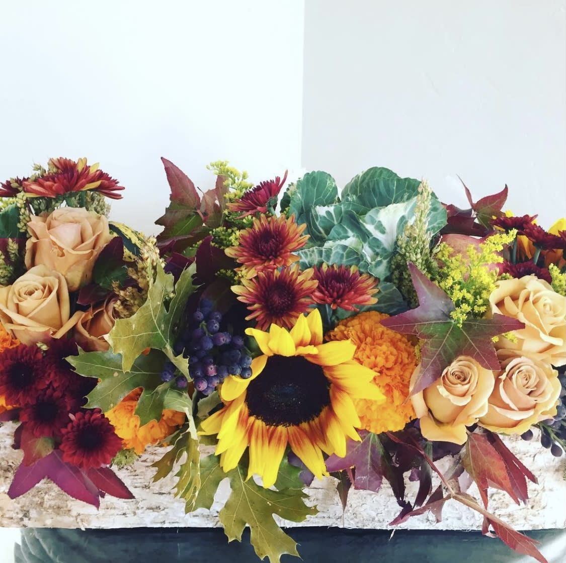 Autumn floral arrangement with sunflowers, roses, and chrysanthemums in a low container