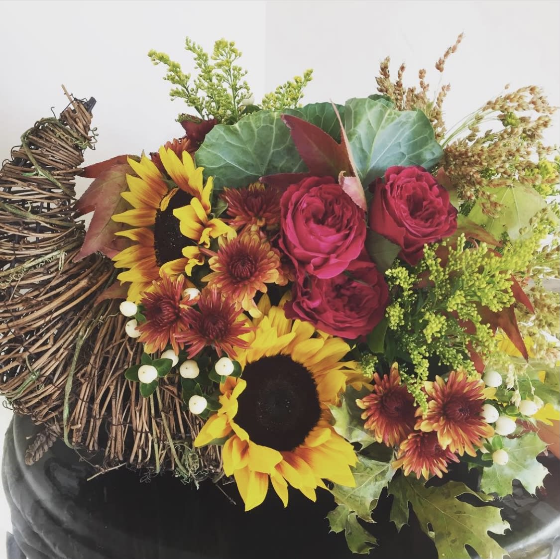 Bouquet with sunflowers, red roses, and autumn foliage in a woven container