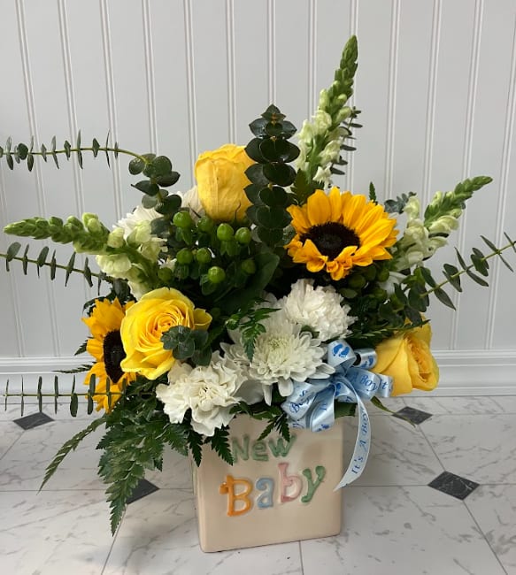 Yellow roses and sunflowers in a baby-themed container with a blue ribbon.