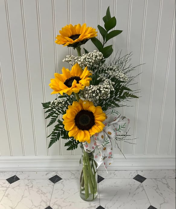 Tall sunflower arrangement in a clear glass vase with a patterned ribbon
