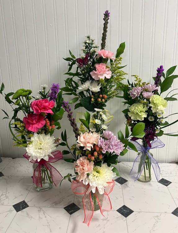 Three mixed flower bouquets in glass vases with ribbon bows