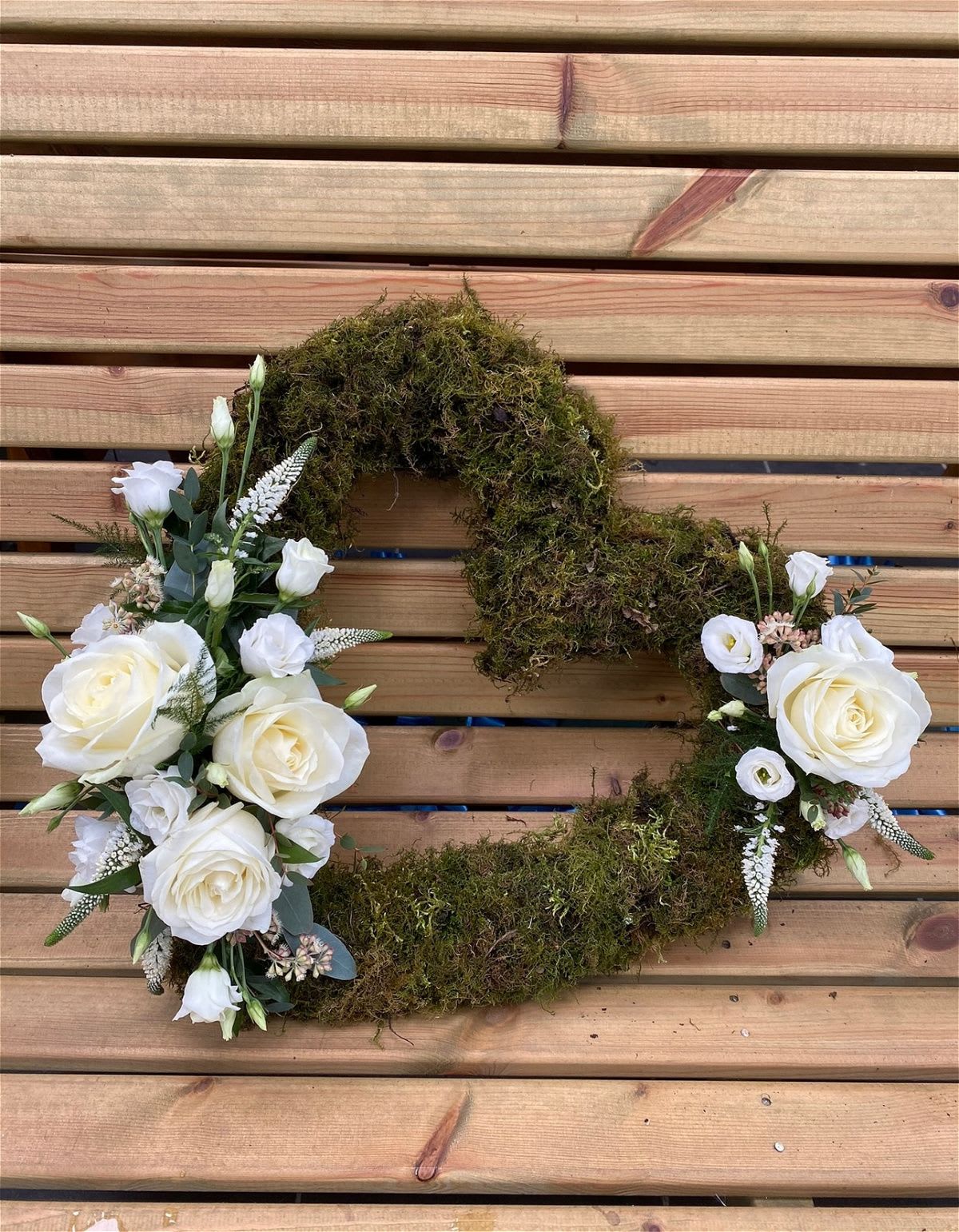 White rose floral wreath with moss on a wooden slat background