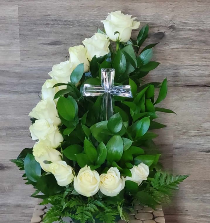 White roses arranged around a clear cross with green foliage