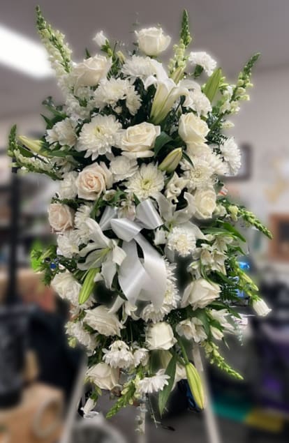 Tall white standing spray with roses, lilies, mums, and snapdragons on a stand with a white bow.