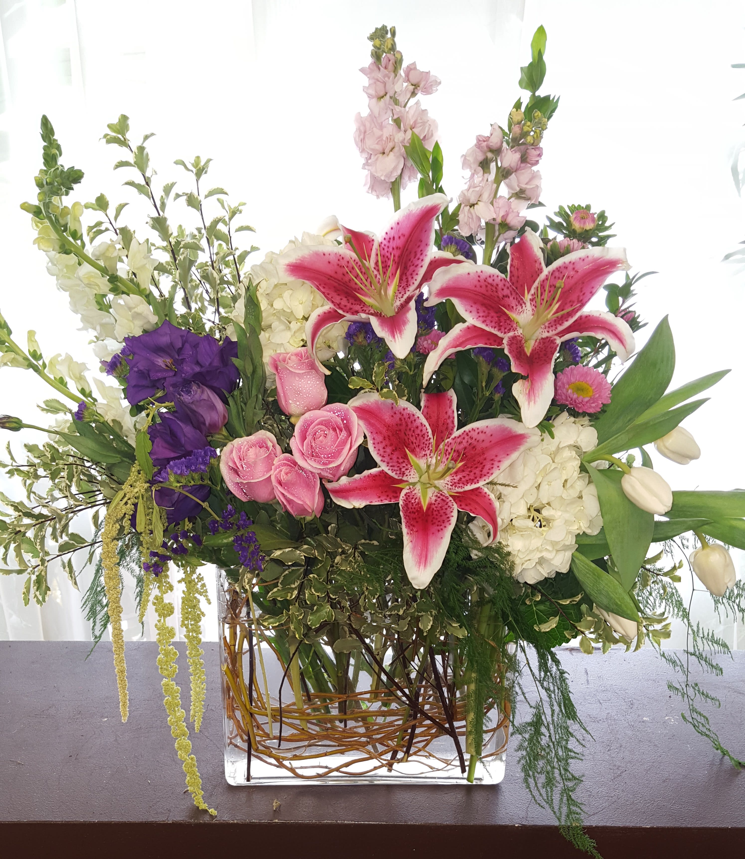 Mixed bouquet with pink lilies, roses, and purple blooms in a glass vase