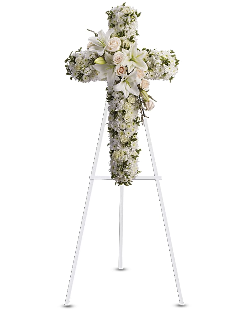 White floral cross on a stand with lilies and roses