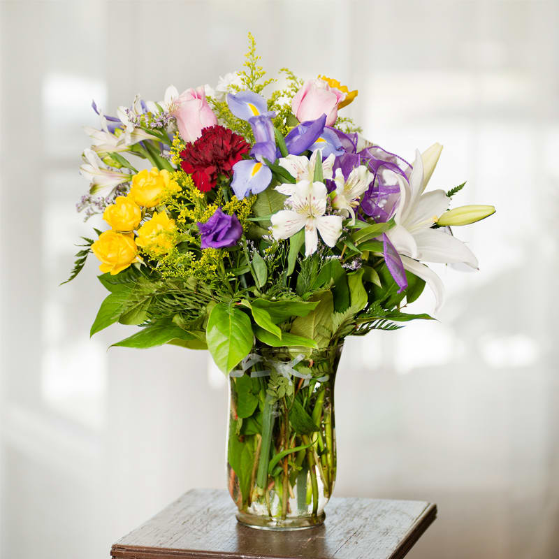 Mixed bouquet of roses, lilies, and irises in a glass vase
