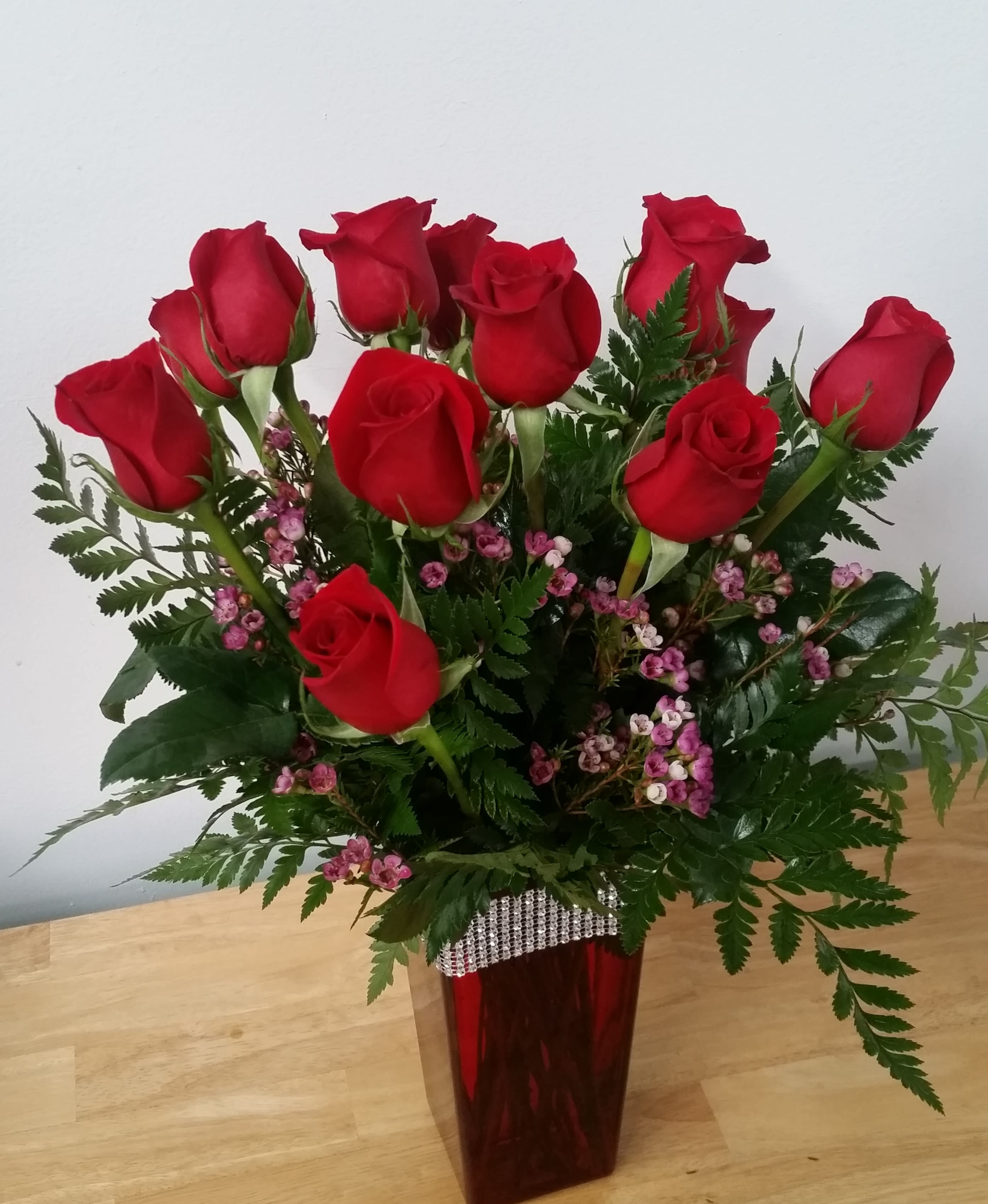 Red roses arranged in a tall vase with pink filler flowers