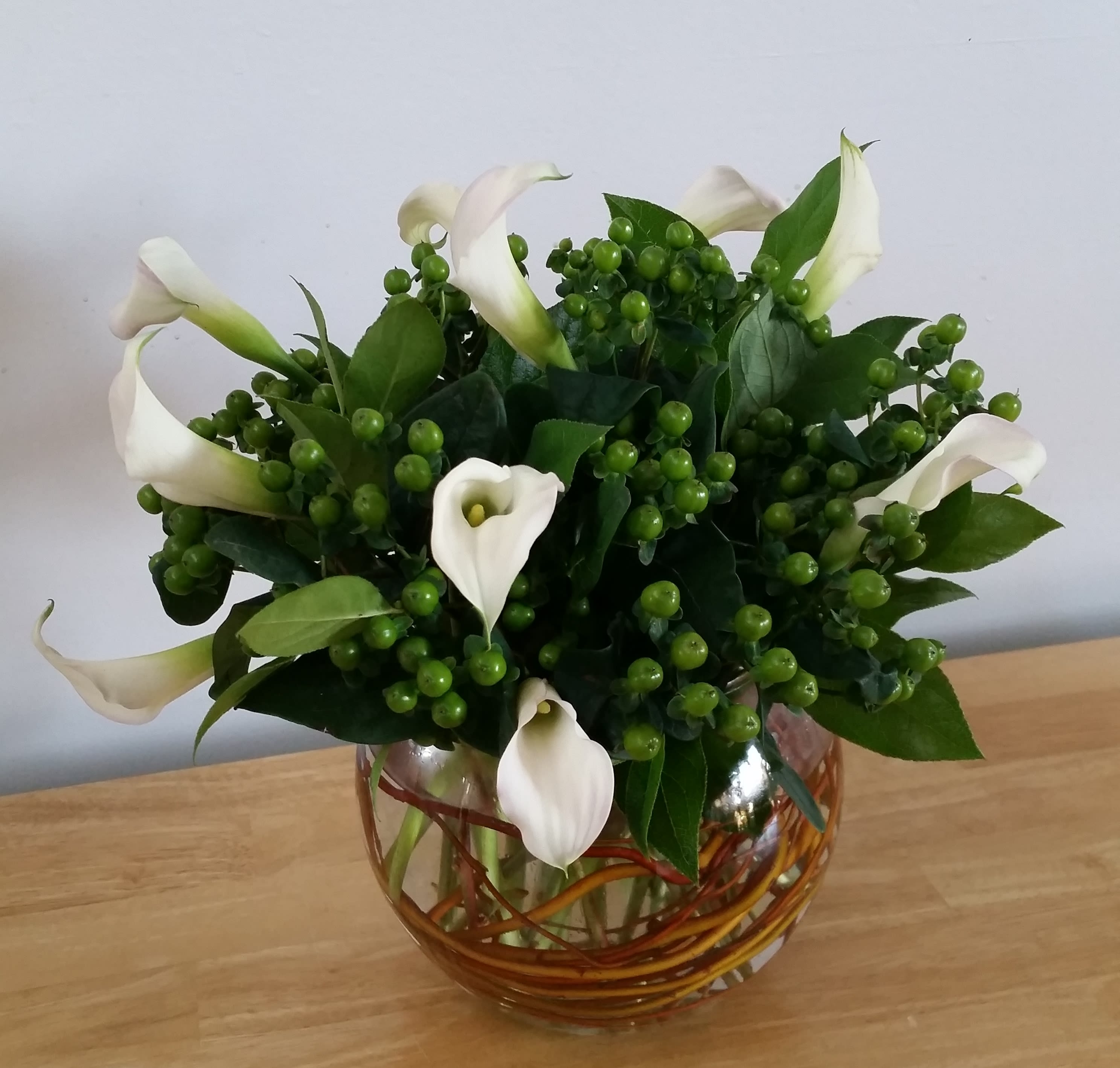 White calla lilies in a glass vase with green berry clusters