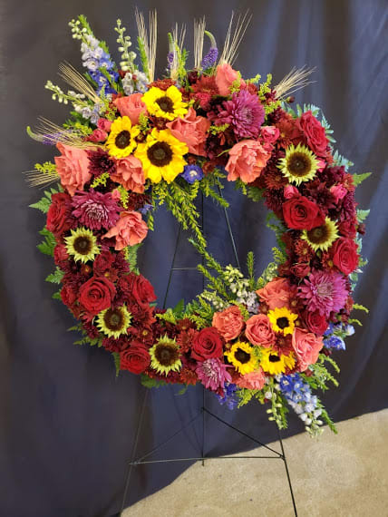 Circular floral wreath with red, pink, yellow, and purple flowers on a stand