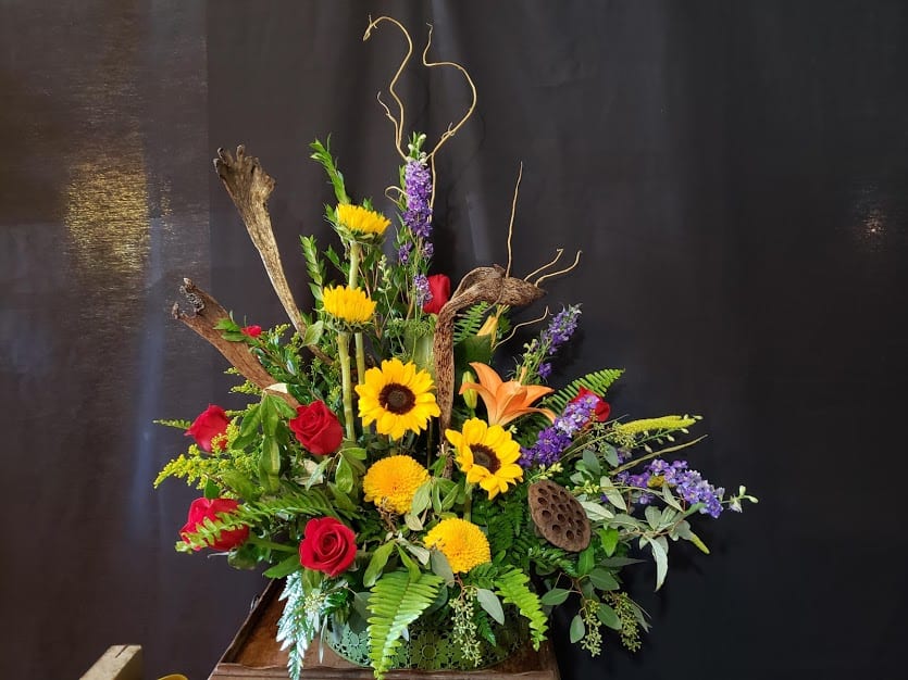 Tall floral arrangement with sunflowers, red roses, and orange lilies