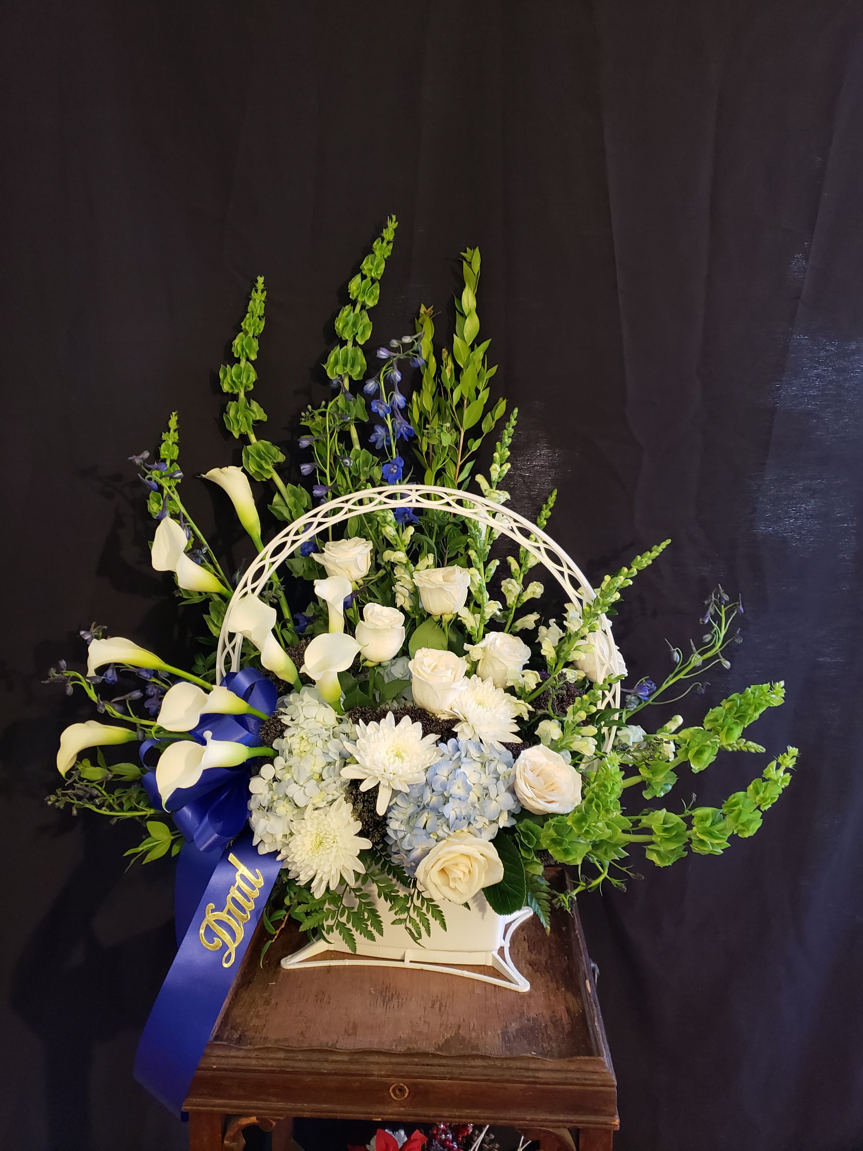 White floral arrangement with calla lilies, roses, and blue ribbon in a basket