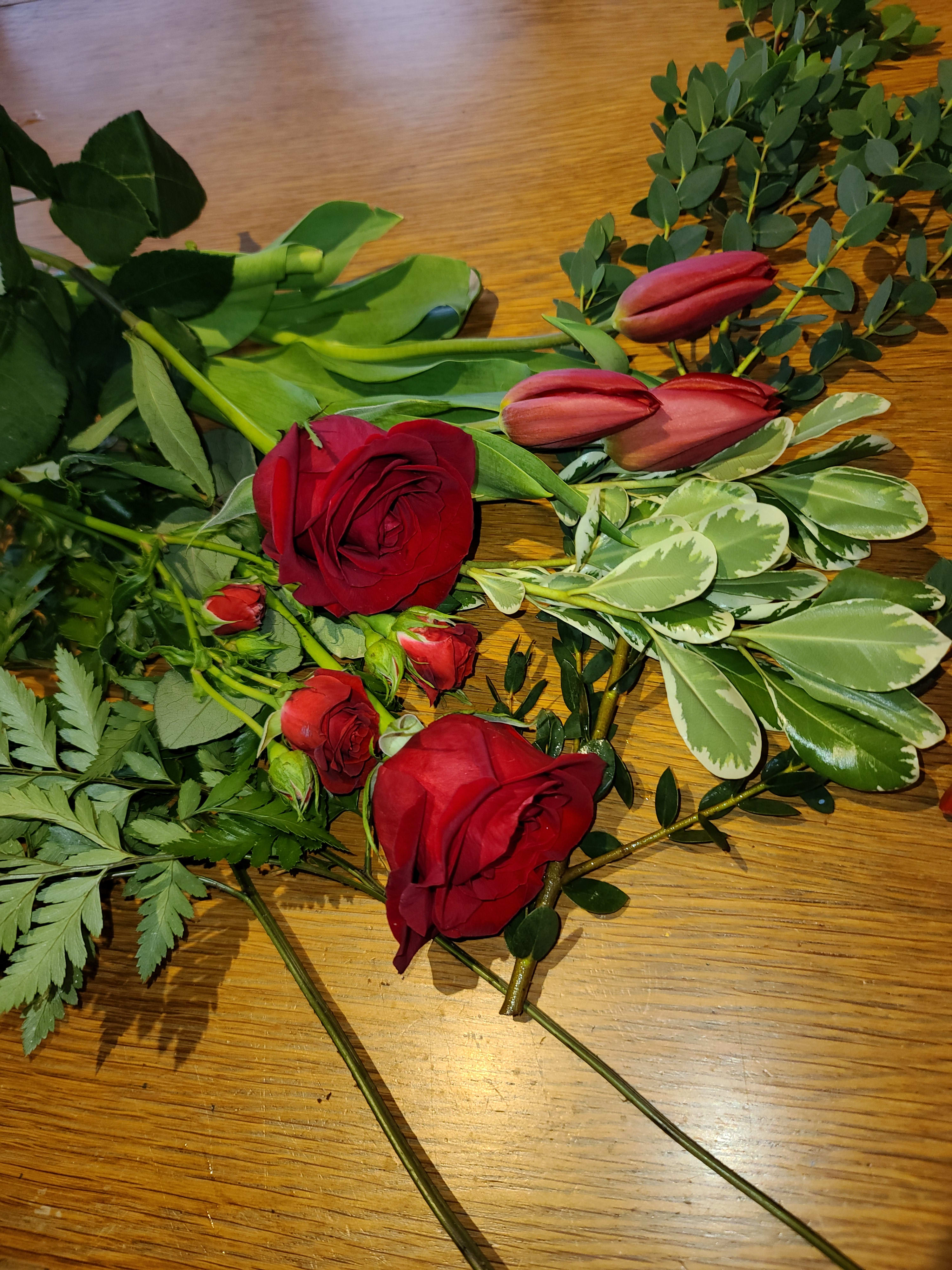 Red roses and pink tulips with assorted greenery on a wooden surface