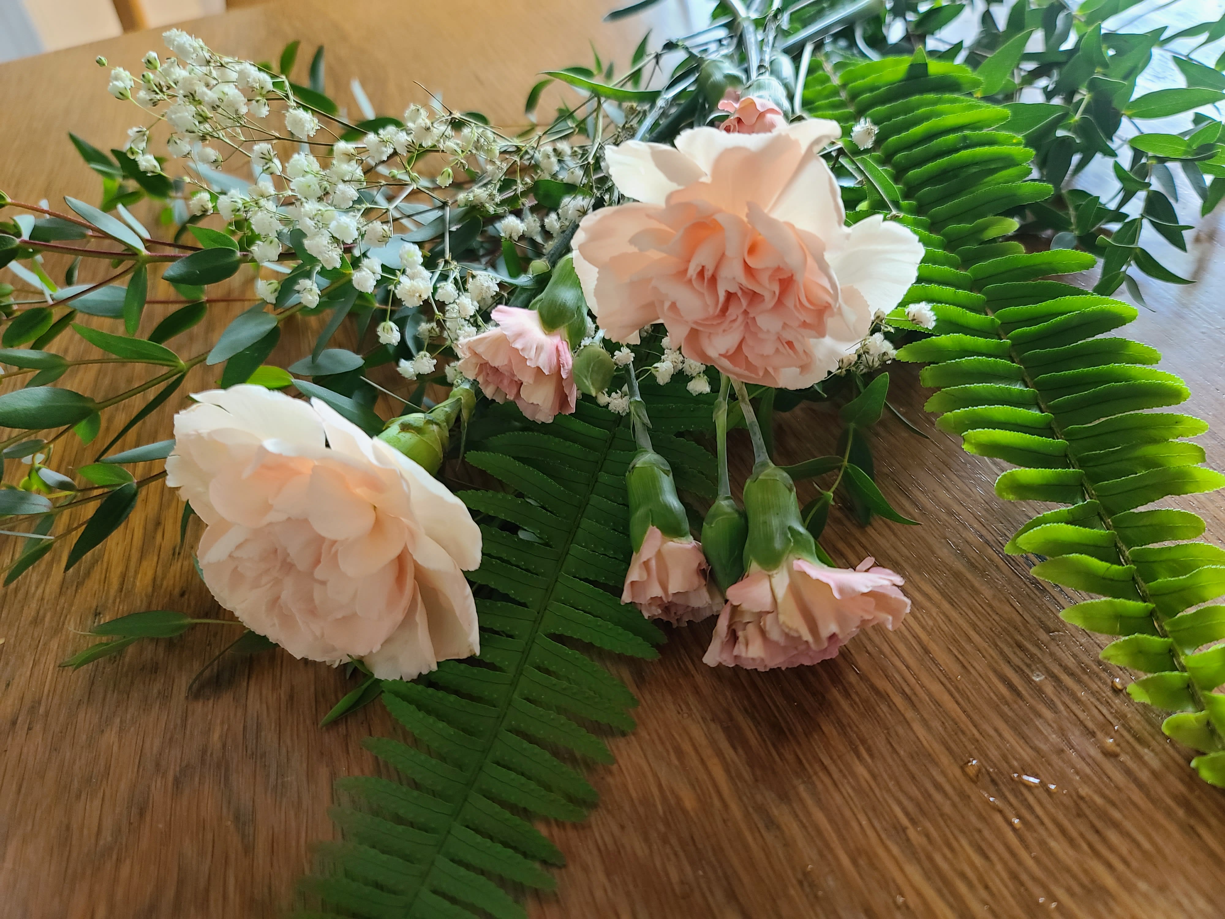 Peach carnations with baby's breath and fern fronds on a wooden surface
