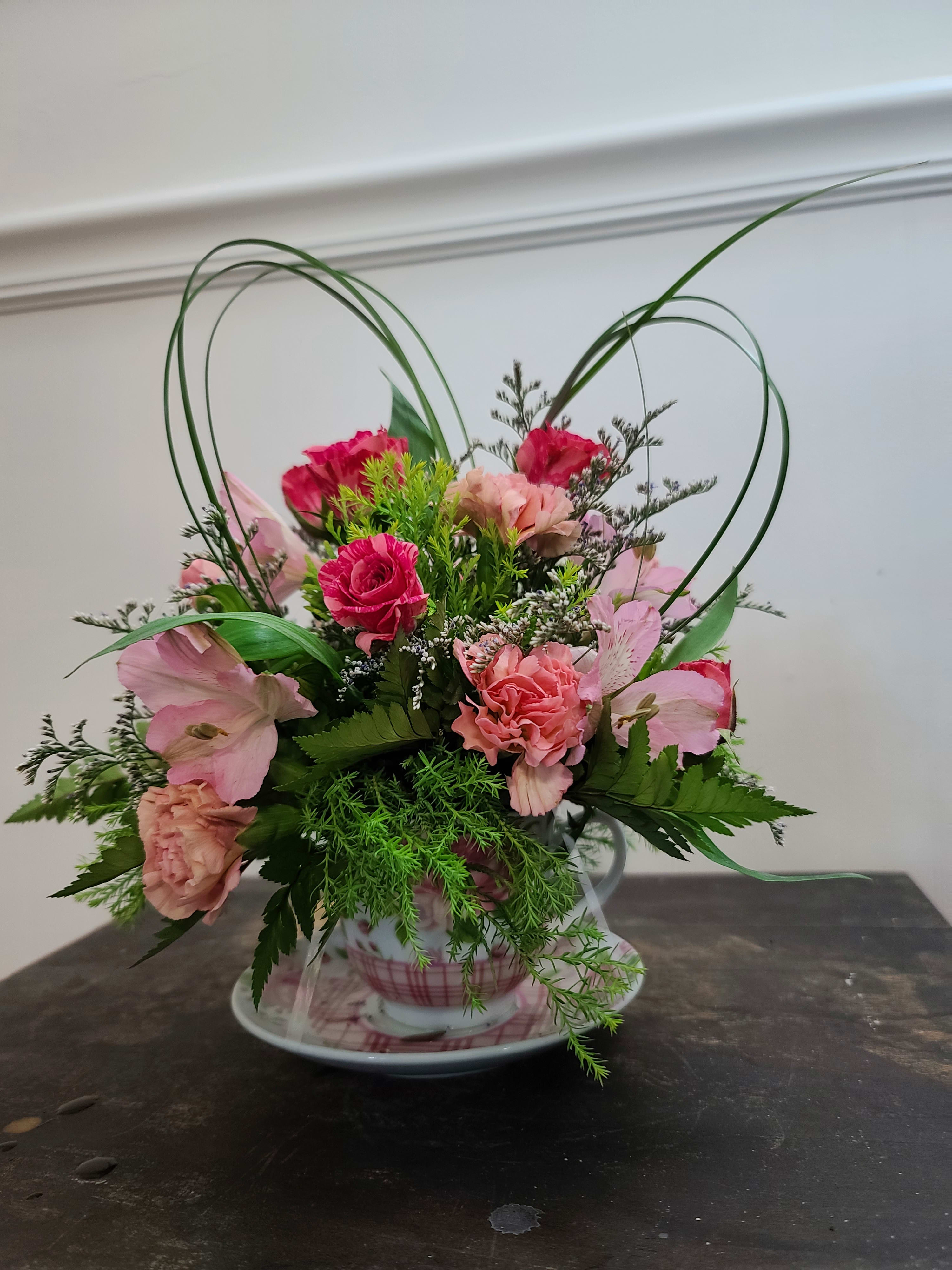 Pink floral arrangement in a teacup with heart-shaped loops