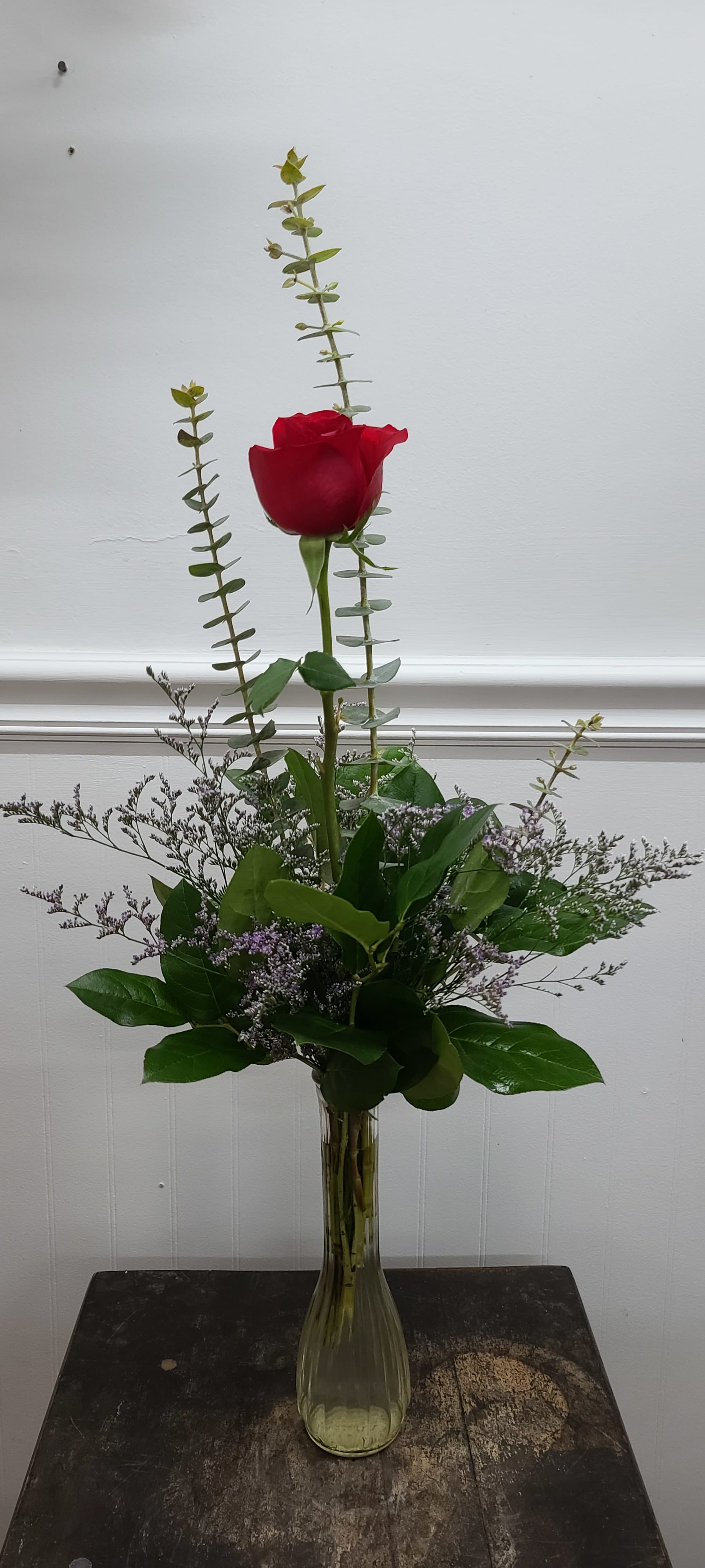 Single red rose in a clear glass vase with tall greenery