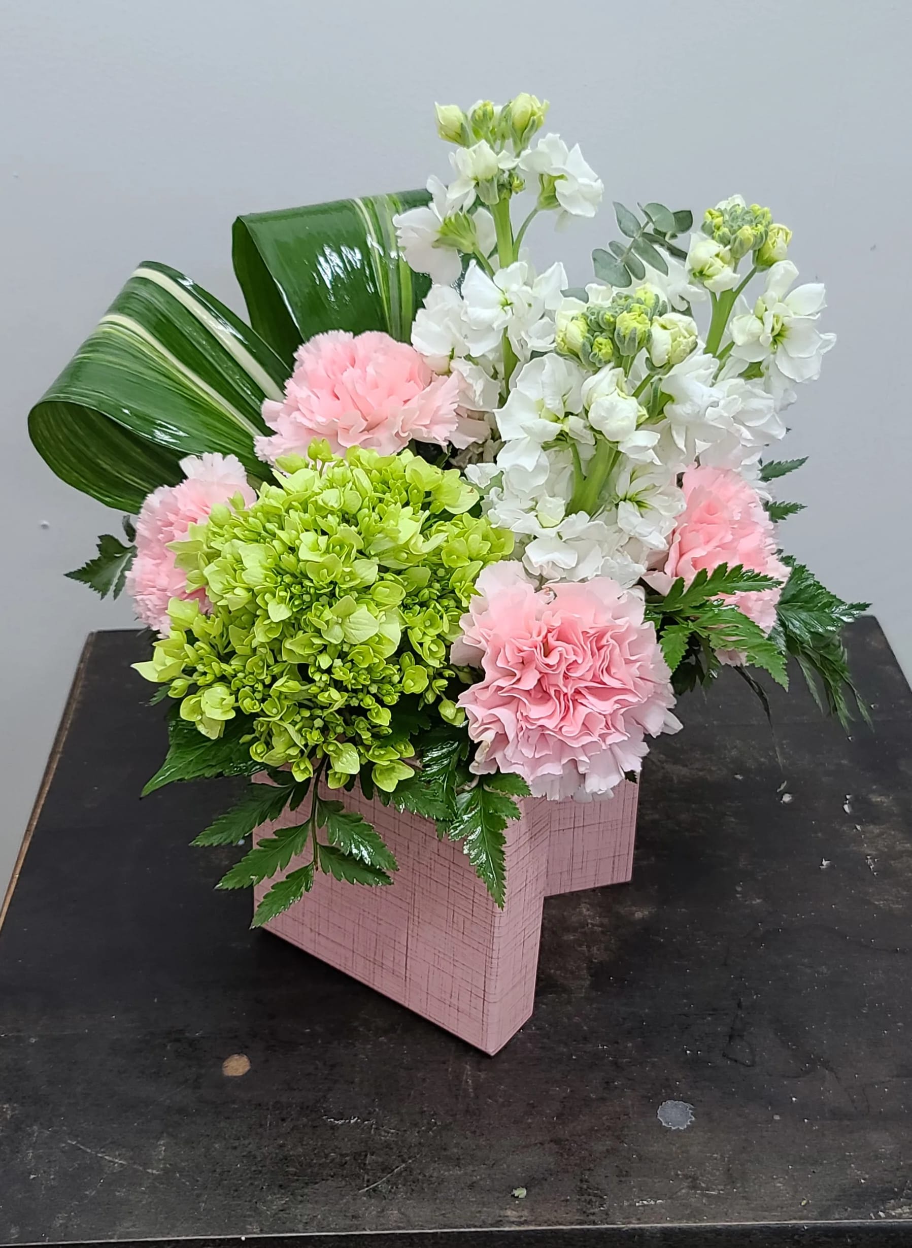 Pink and white floral arrangement in a pink box with green accents