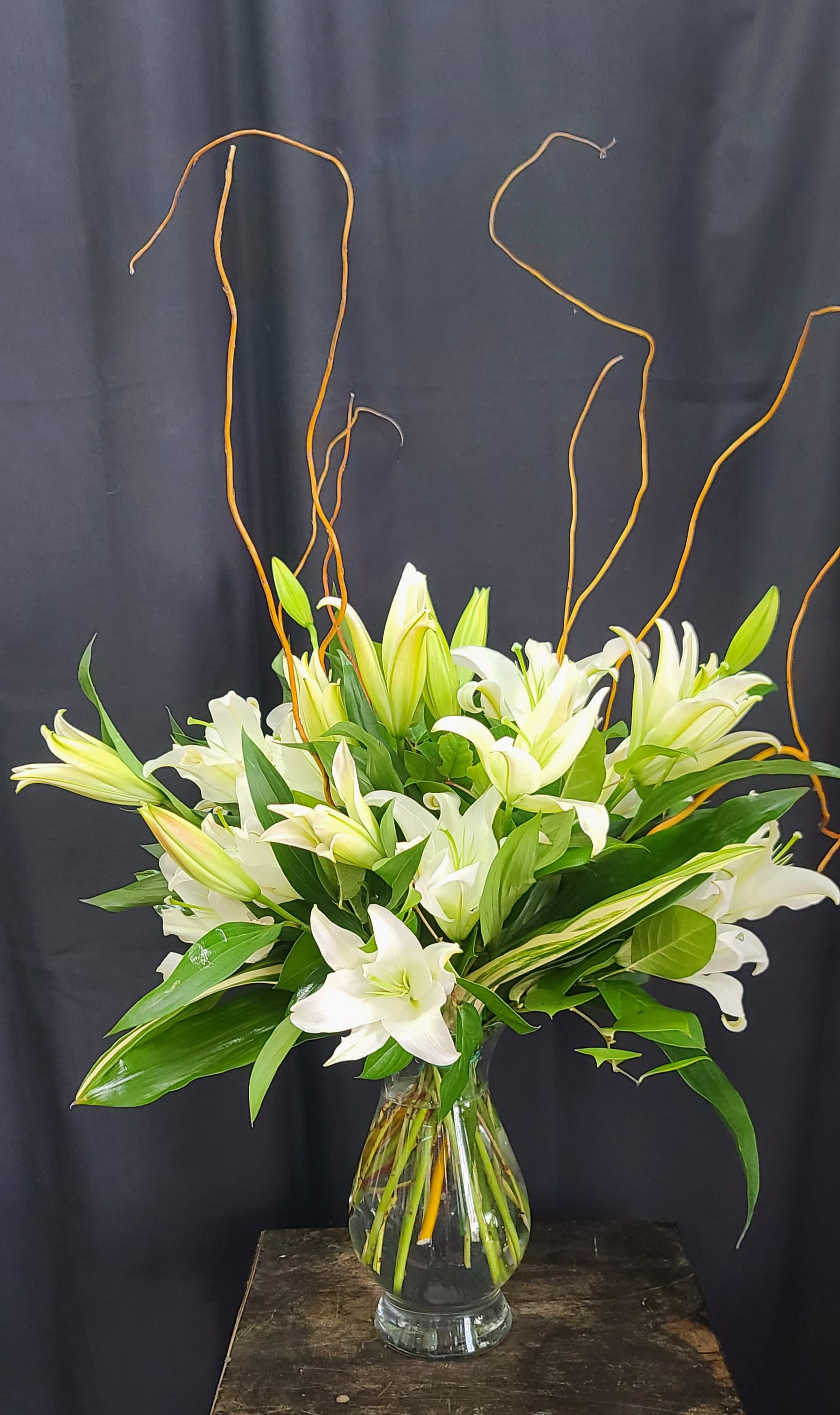 White lilies arranged in a clear glass vase with curly branches