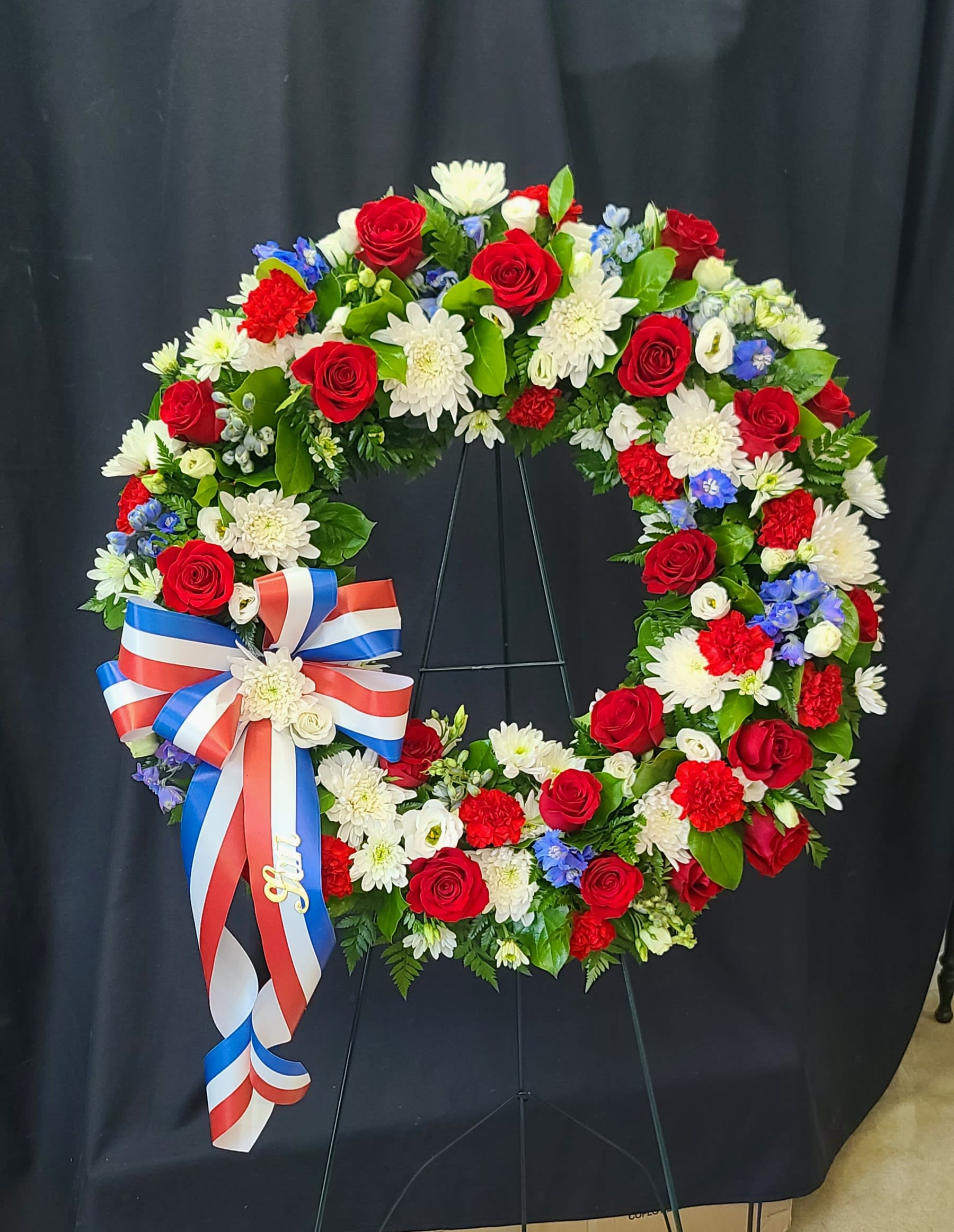 Circular wreath of red, white, and blue flowers with a ribbon bow