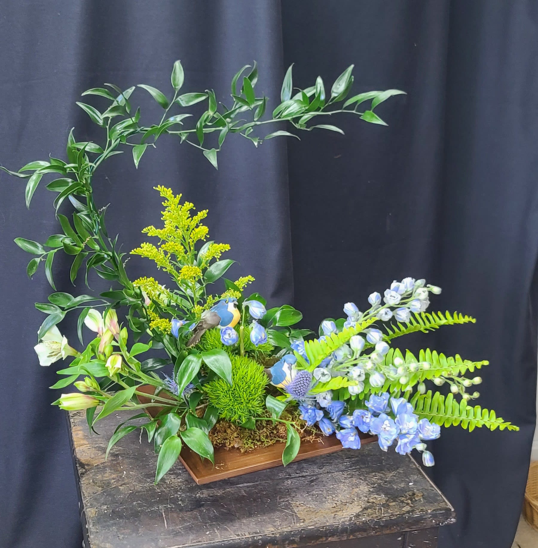 Floral arrangement with blue and white blooms in a wooden tray