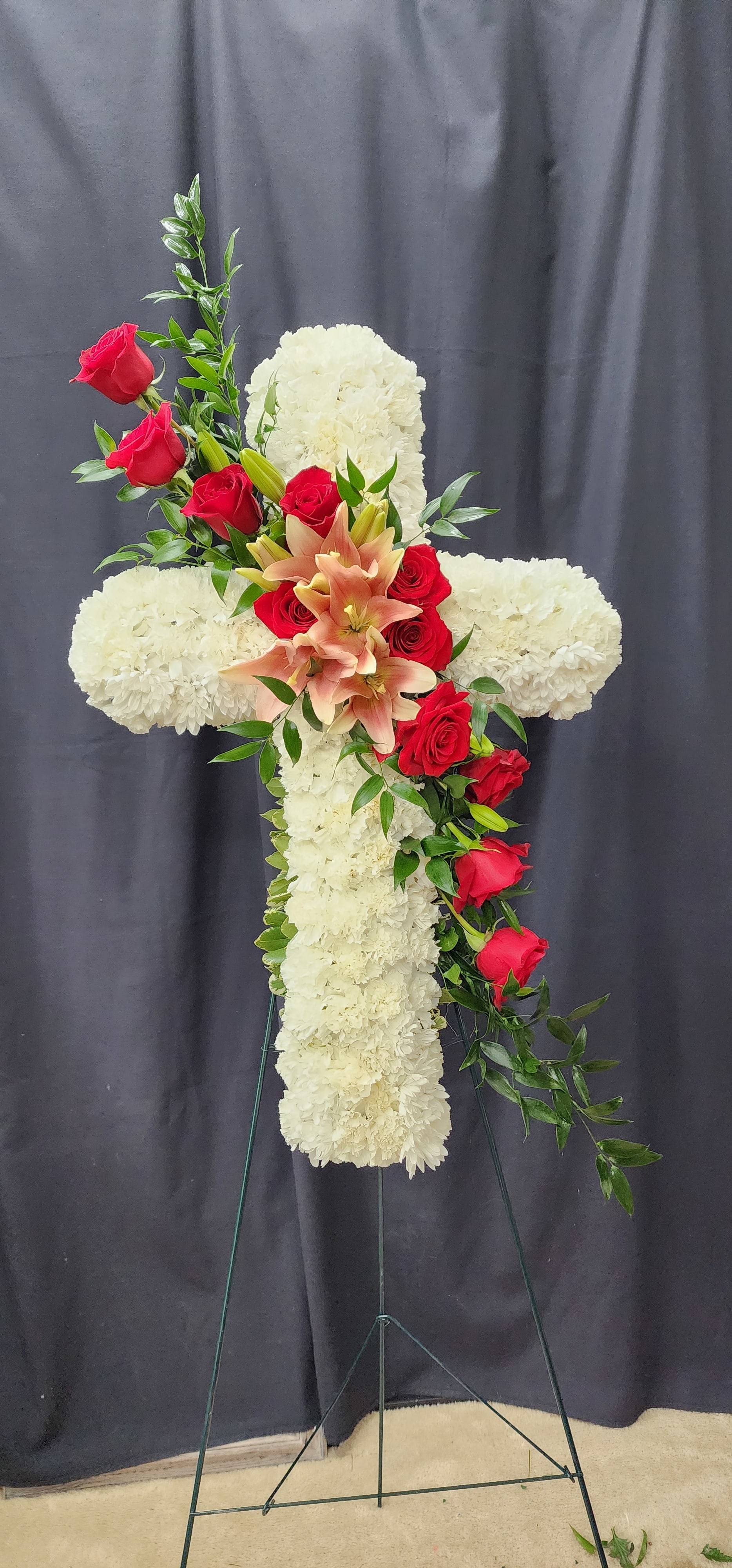 White floral cross with red roses and peach lilies on a stand
