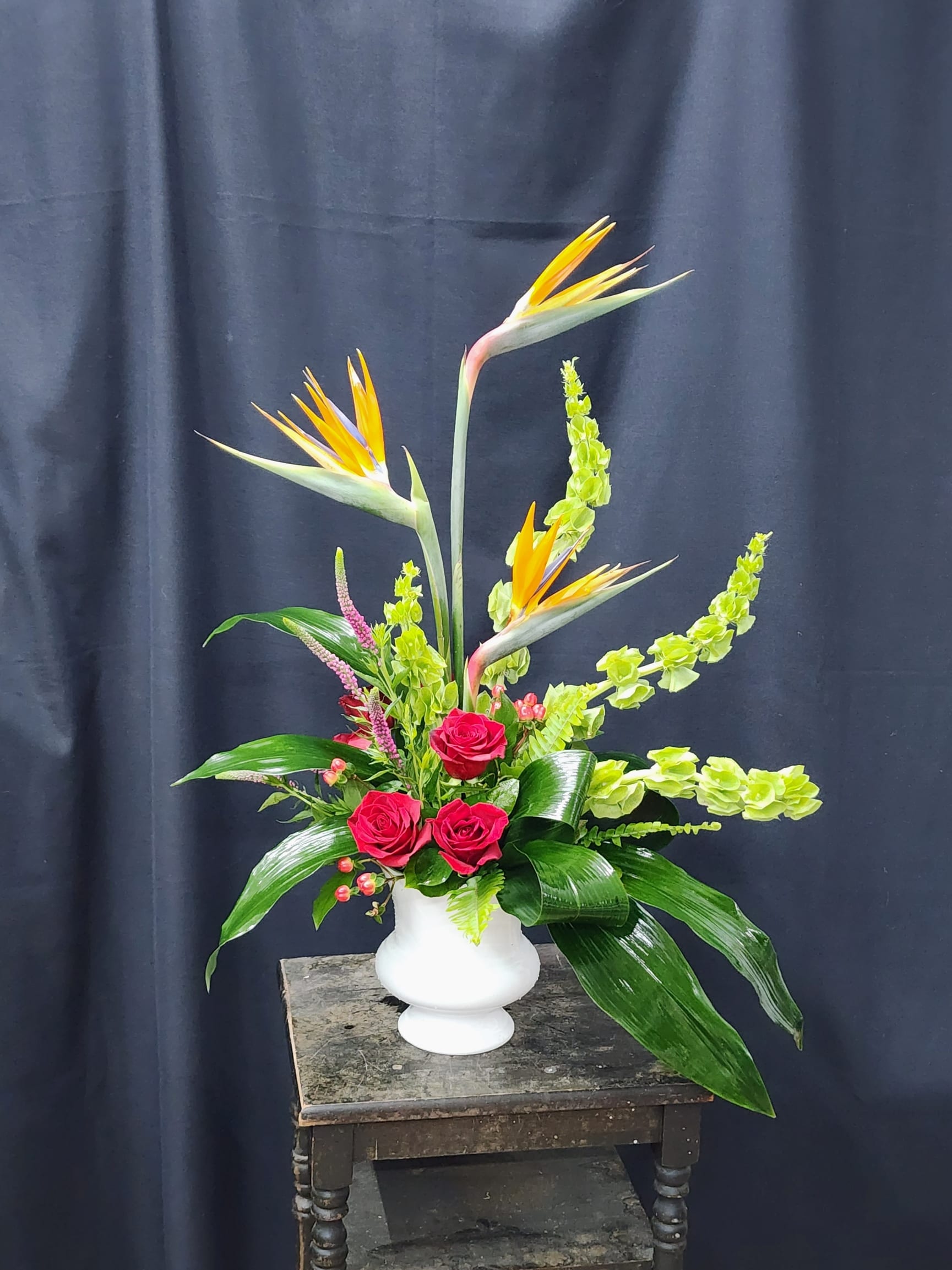 Tall tropical arrangement with red roses and bird of paradise in a white vase