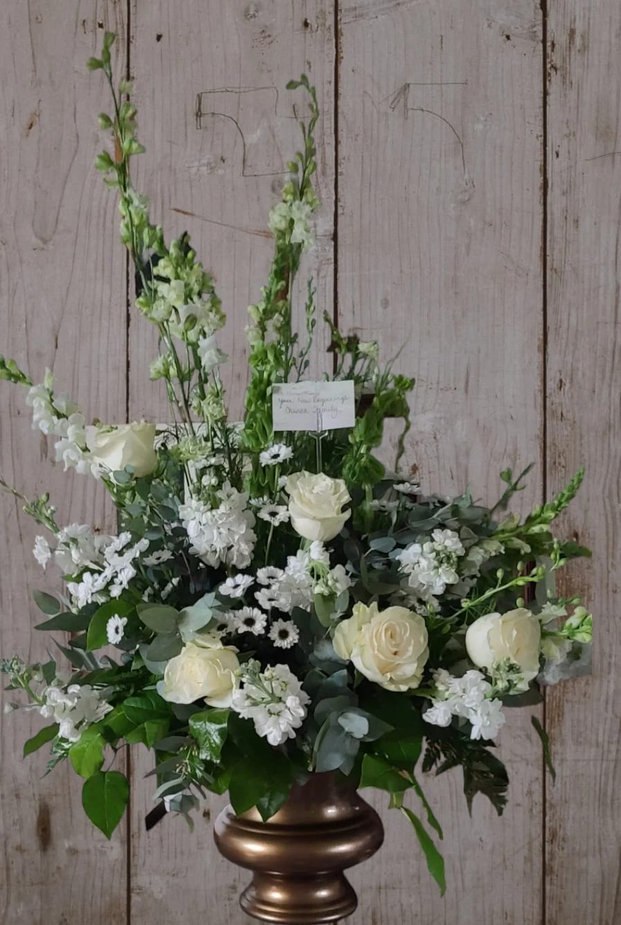 White floral arrangement with roses and tall snapdragons in a bronze vase