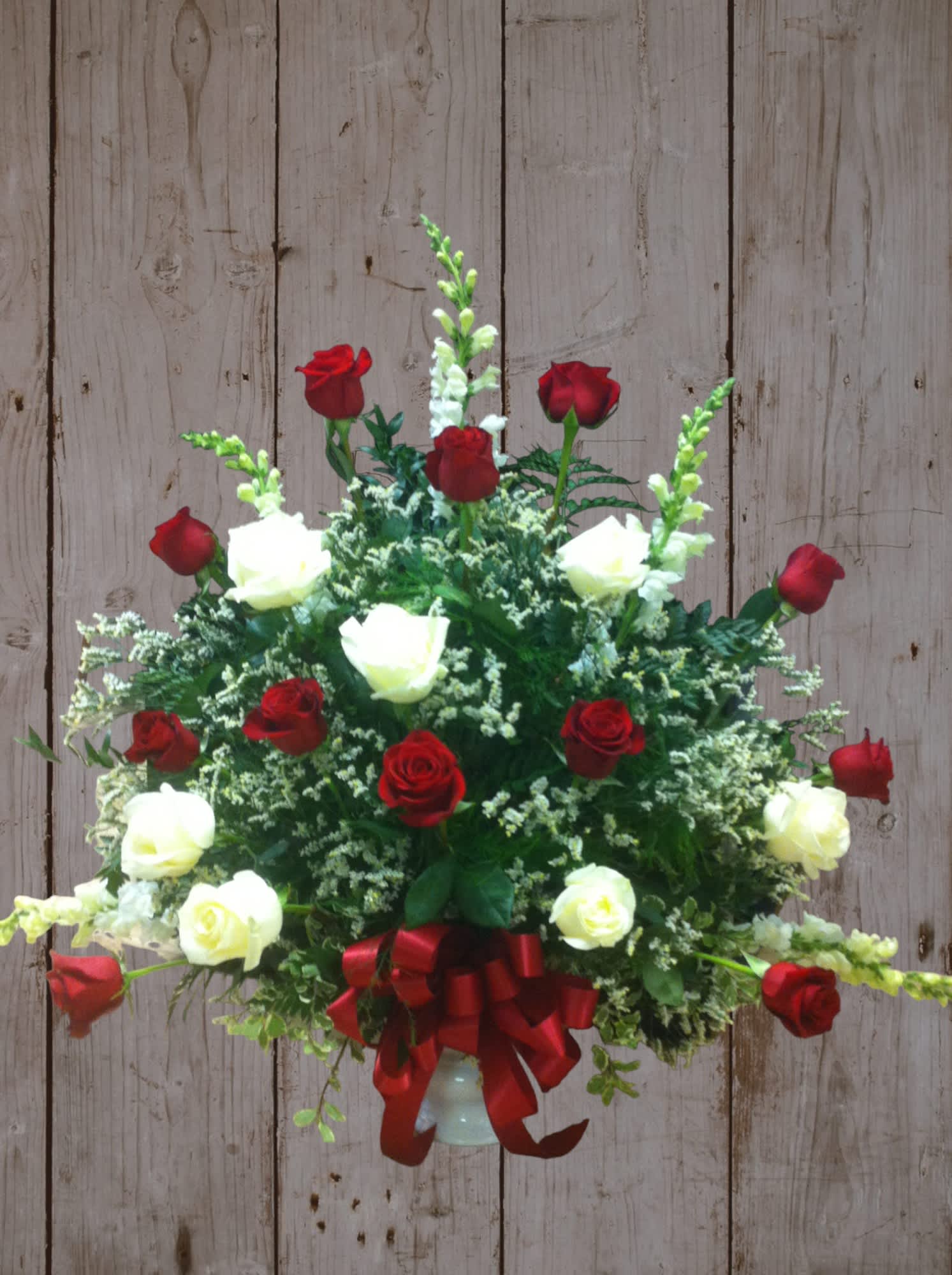 Red and white roses arranged in a vase with a red ribbon