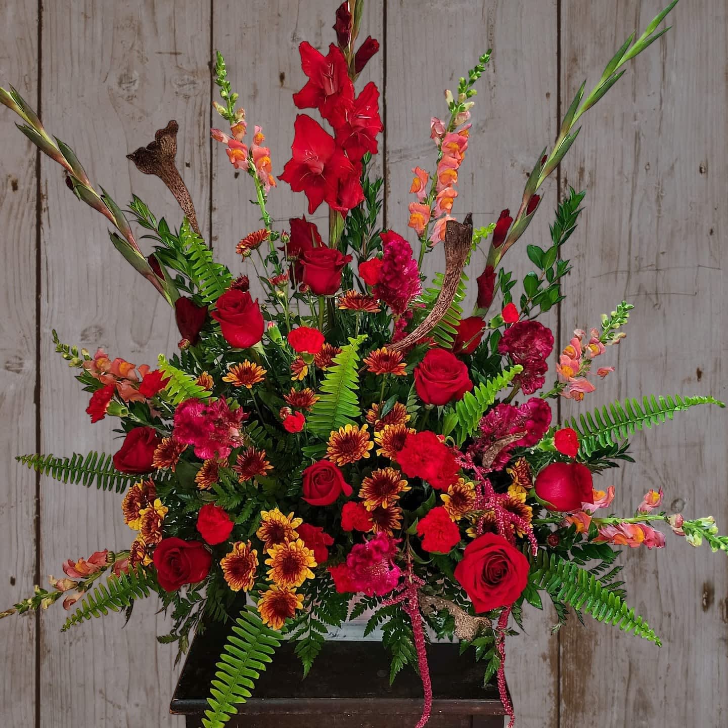 Large red floral arrangement with roses and tall gladiolus in a black container